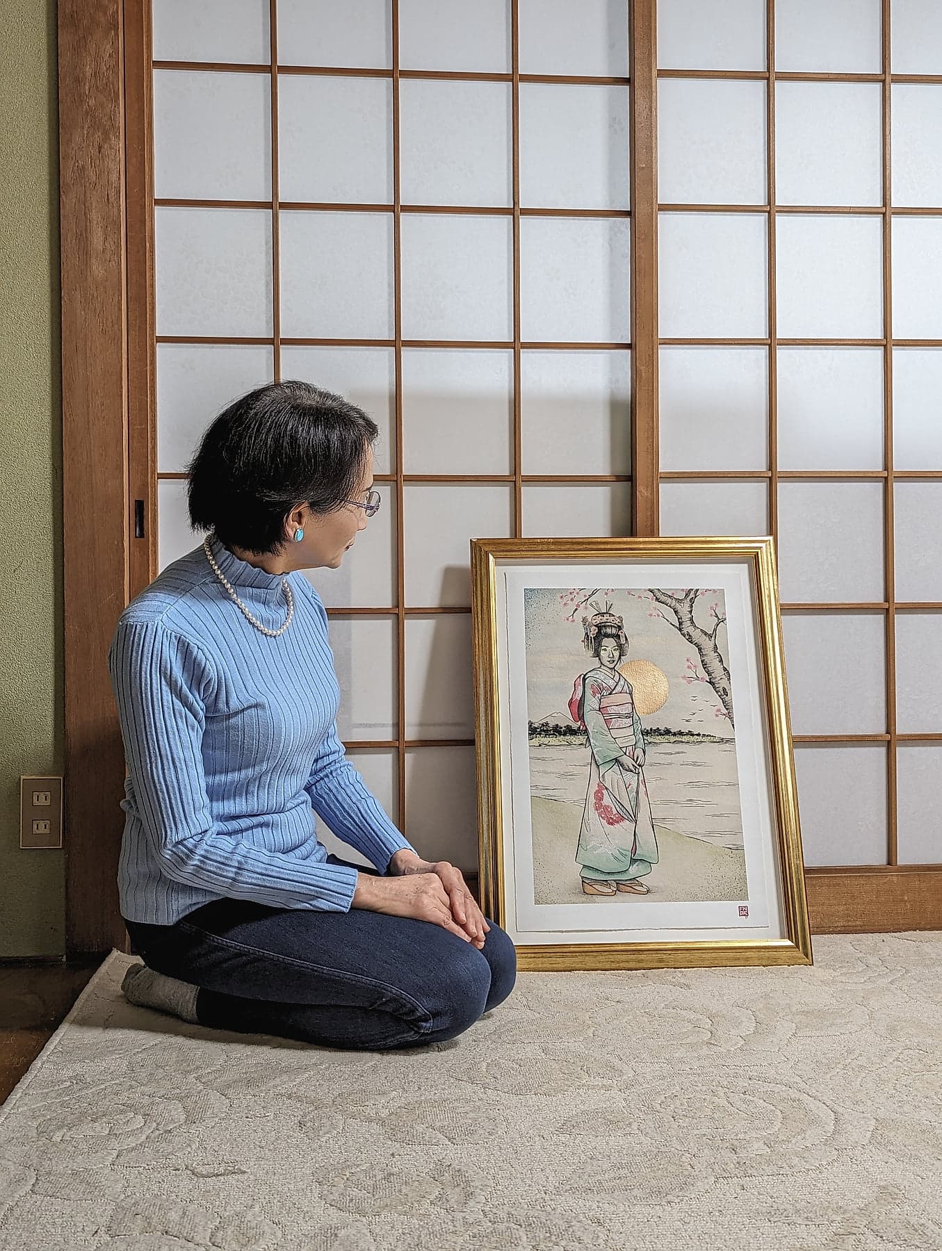 Mitsuko sitting in seiza beside the framed portrait in her tatami room in Japan, shoji screens behind her