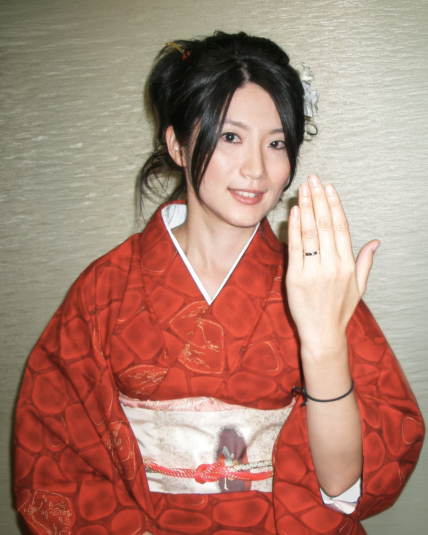 Rieko on her wedding day in Japan in 2009, wearing a red silk kimono with a white flower pinned in her hair, holding up her hand to show her wedding ring