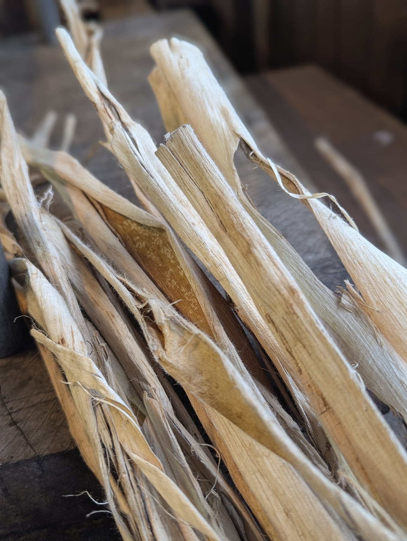Strips of dried kozo mulberry bark fibre on a worn wooden surface in the workshop