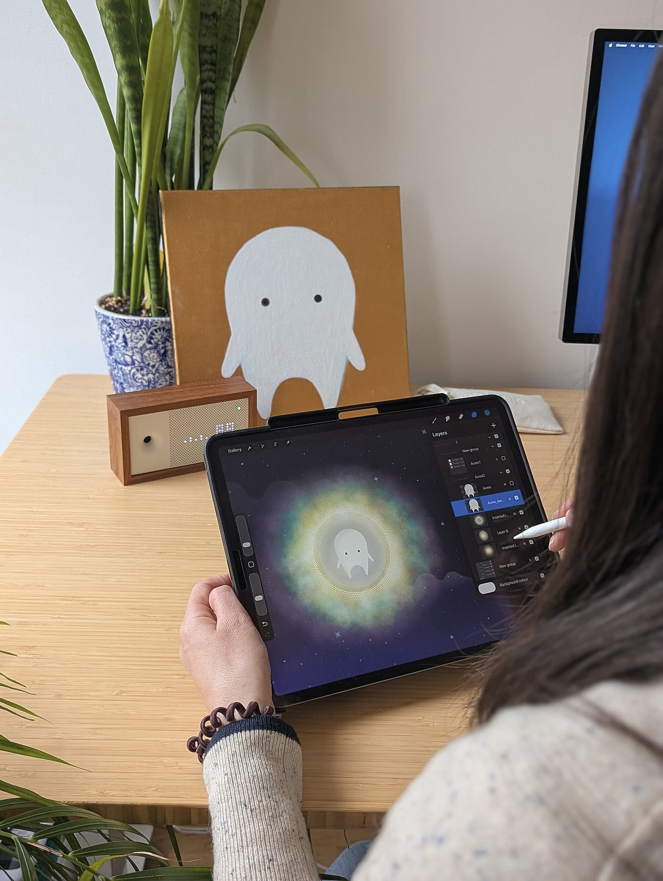 Drawing Auwa in Procreate on an iPad Pro with Apple Pencil, the original gold canvas painting of the character visible on the desk behind