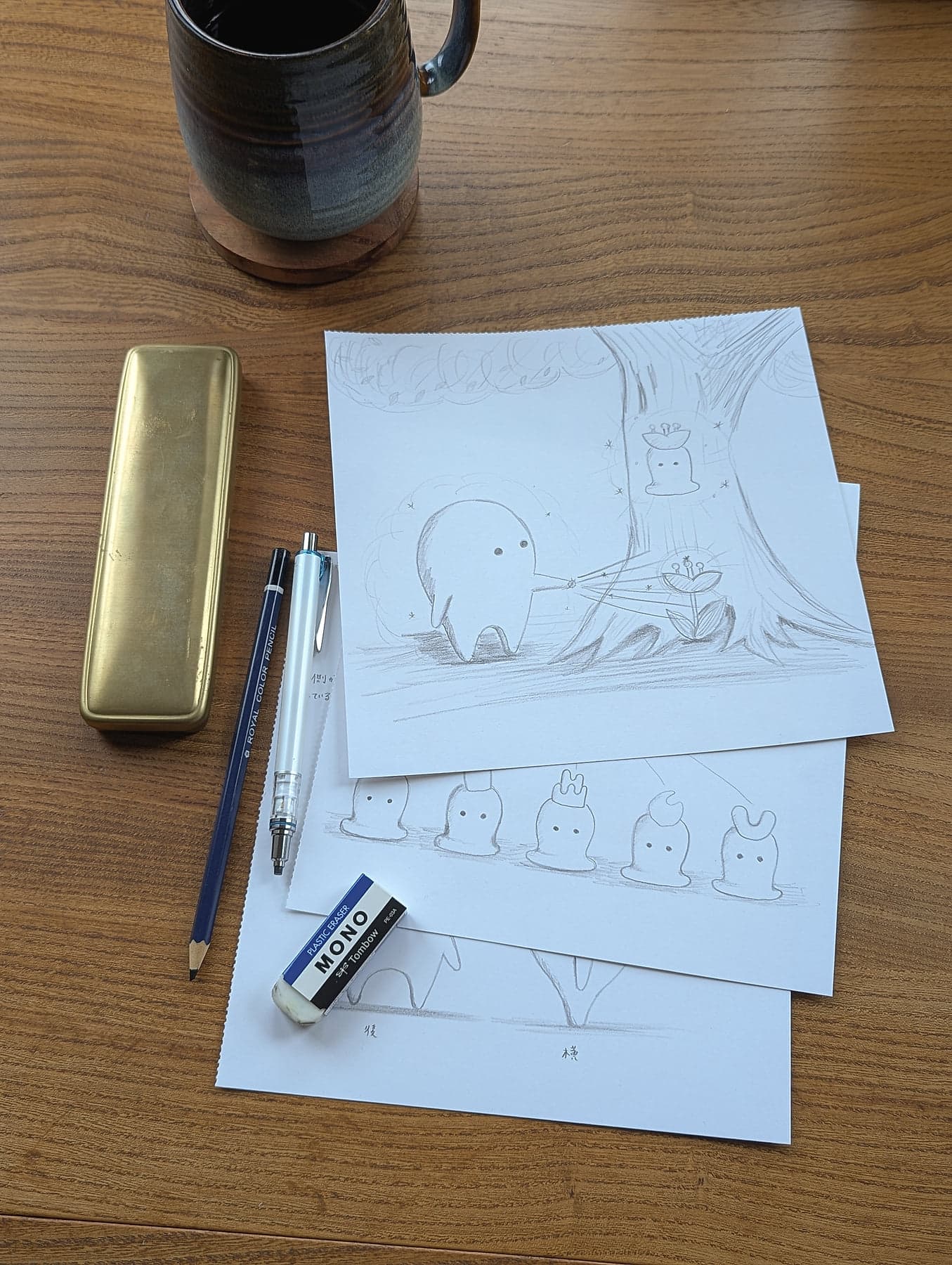 Pencil sketches of Auwa character scenes by Japanese illustrator Rieko Maeda, laid out on a wooden desk with a MONO eraser, mechanical pencil, and brass pencil case