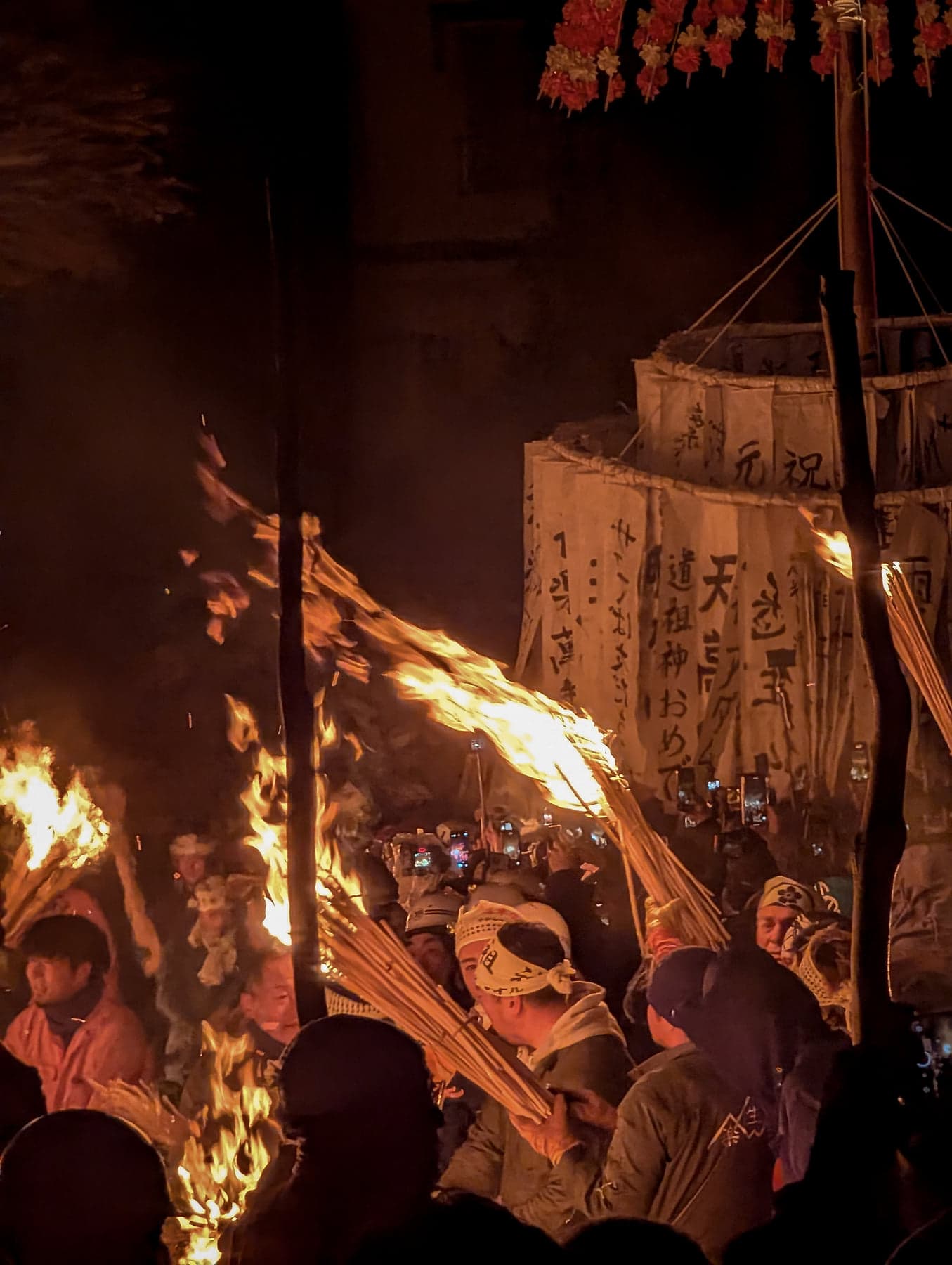 Close-up of villagers wielding torches beneath kanji-painted banners at the Dosojin Matsuri fire festival