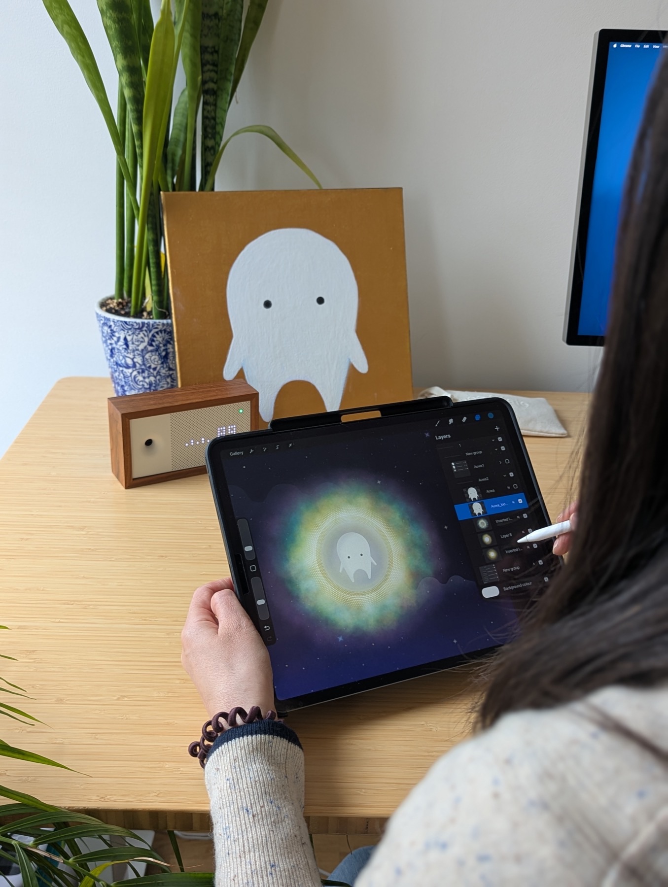 Drawing AUWA in Procreate on an iPad Pro with Apple Pencil, the original gold canvas painting of the character visible on the desk behind