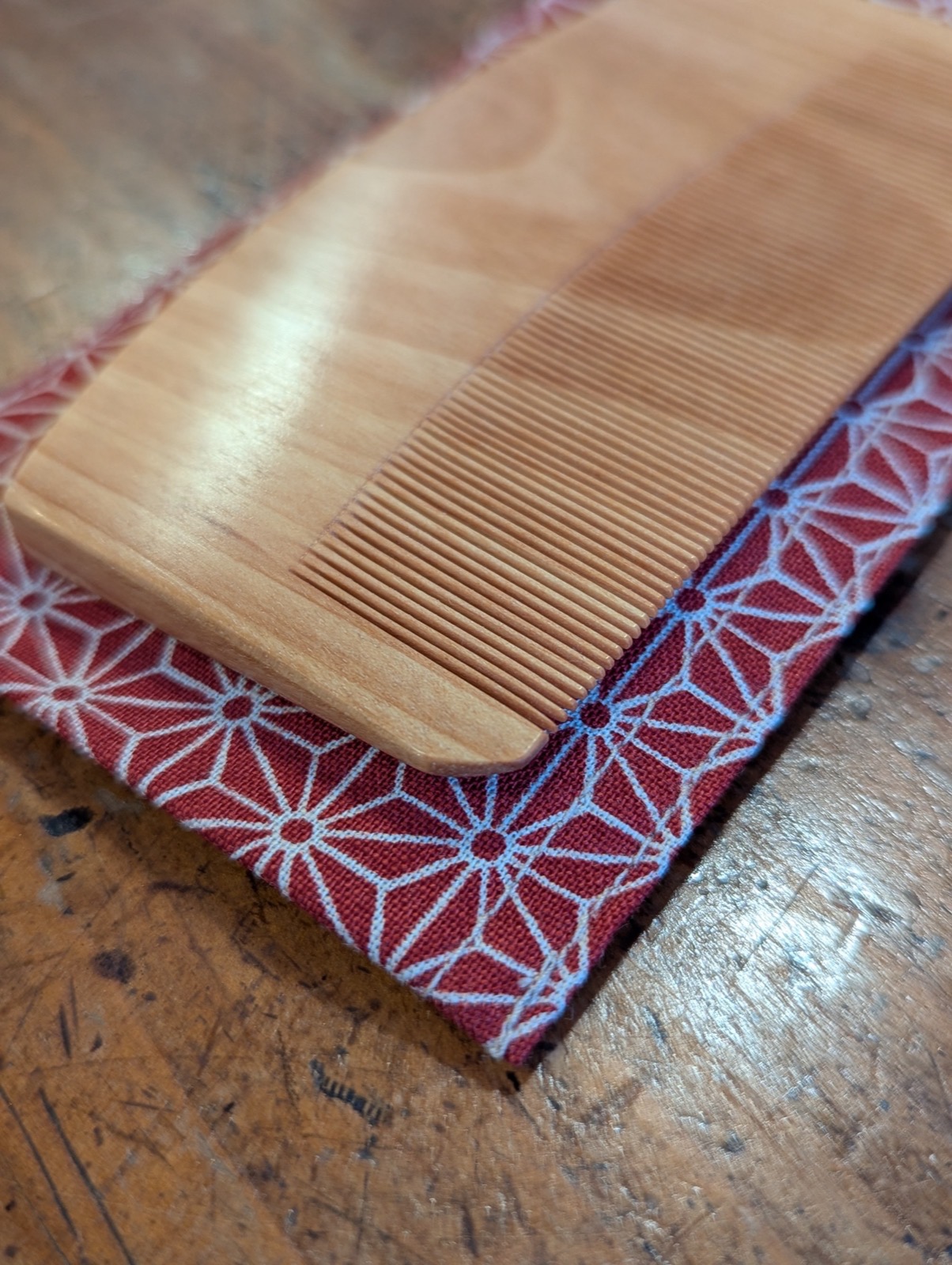 Close-up of an oroku-gushi comb showing finely cut minebari wood teeth emerging from its asanoha-patterned cotton pouch