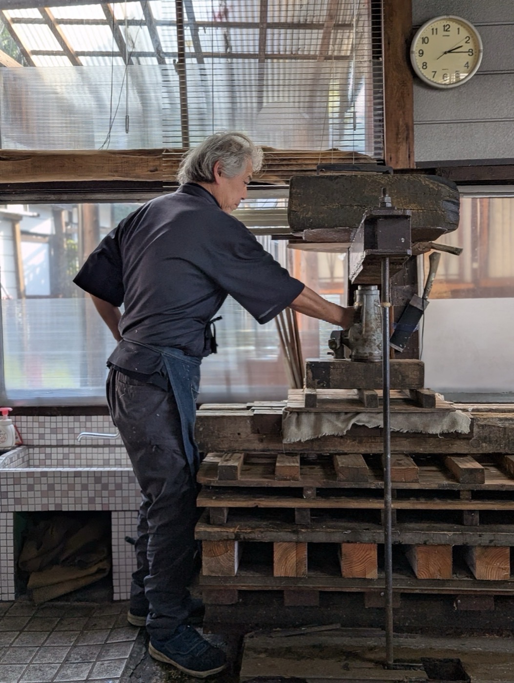Matsuzaki-san operating the heavy wooden screw press to squeeze water from freshly formed washi sheets